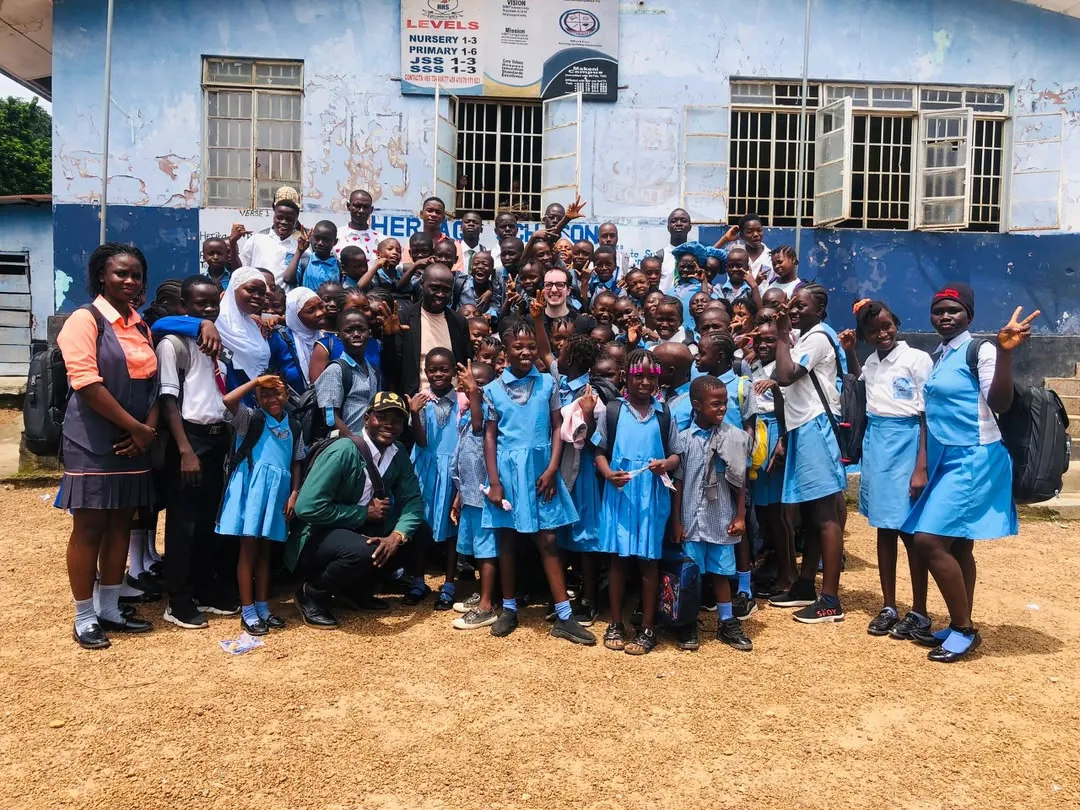 Max standing with a group of students and their teachers outside a partner school